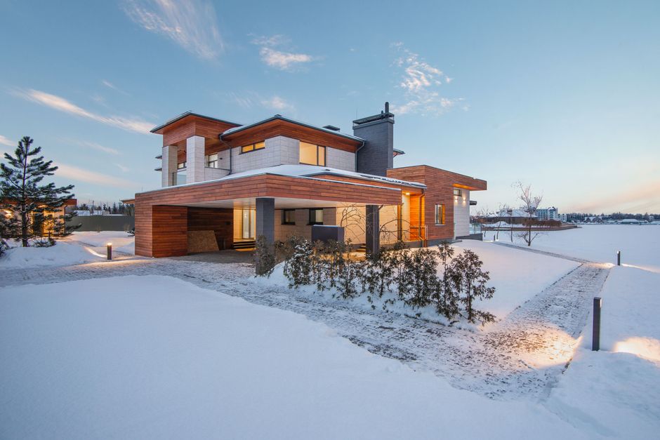 Exterior view of luxurious residential house with roofed parking and spacious backyard in snowy winter countryside